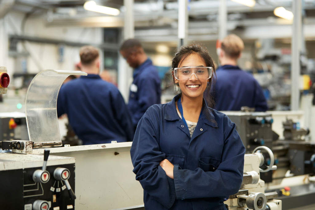Junge Frau im Overall in einer Werkstatt guckt lächelnd in die Kamera